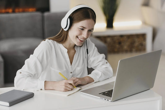 une employée qui prend un cours de langue en ligne avec casque sur les oreilles et qui prend des notes