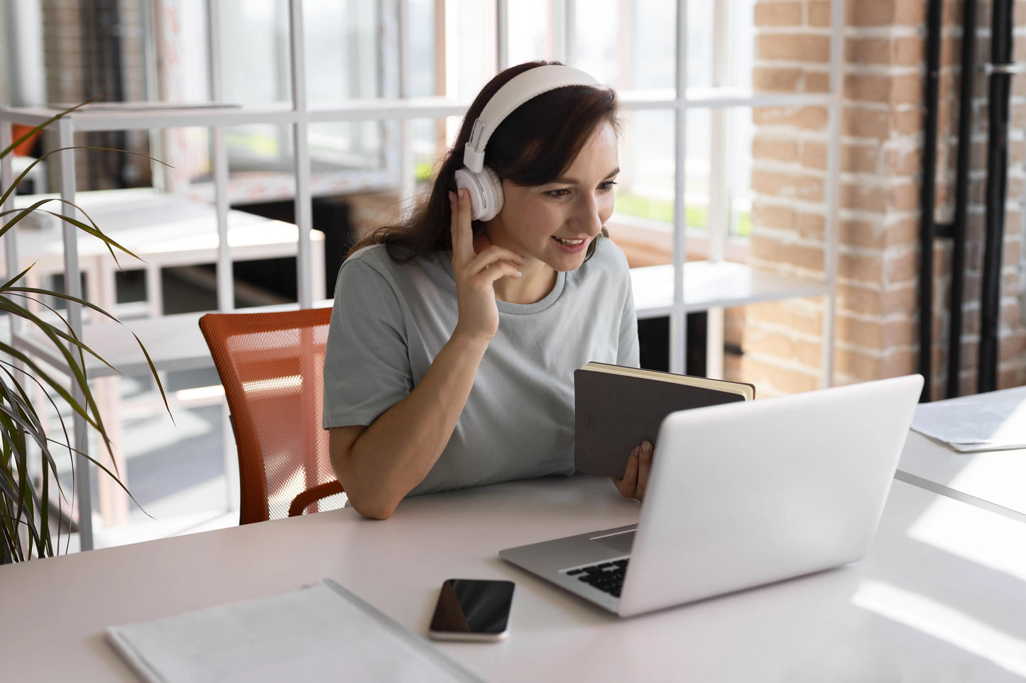 étudiante qui suit un cours en viso avec casque sur la tête devant son pc avec un livre à la main